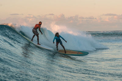 People enjoying in sea against sky during sunset