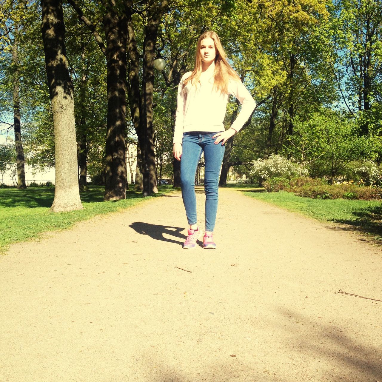 full length, tree, casual clothing, person, lifestyles, young adult, leisure activity, front view, young women, looking at camera, portrait, standing, walking, grass, sunlight, growth, park - man made space, day