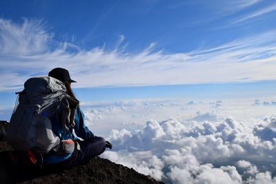 Hiker with backpack sitting on cliff against cloudy sky