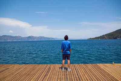 Rear view of man walking on pier over sea against sky