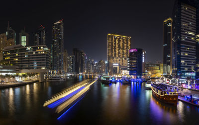 Illuminated buildings by river against sky at night