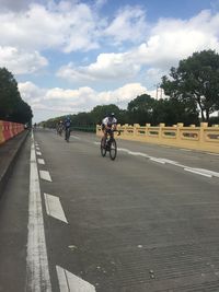 People riding bicycle on road against cloudy sky