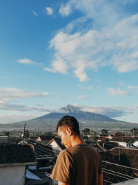 Rear view of man standing by buildings against sky