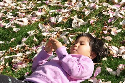 Low angle view of girl on grass with pink petals