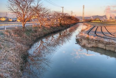 Reflection of bare trees on river against sky