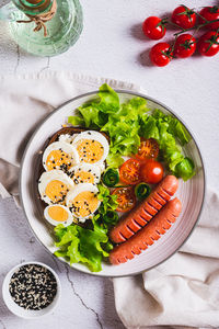 Plate with sausages, egg sandwich, tomatoes and lettuce leaves on the table top and vertical view