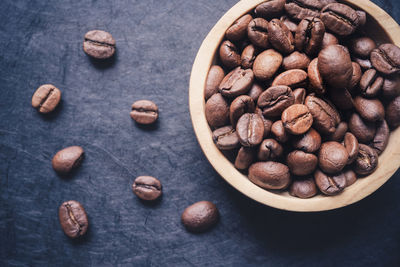 Close-up of a wooden bowl filled with roasted coffee bean on a dark slate background. copy space 