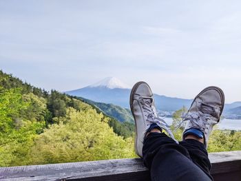 Low section of man relaxing on mountain against sky