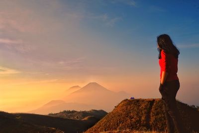 Woman standing on mountain against sky during sunset