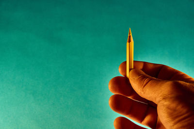 Close-up of hand holding pencils against blue background