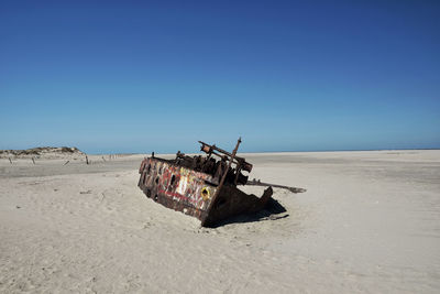 Damaged boat on beach against clear blue sky