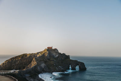 Lighthouse on rocks by sea against clear sky