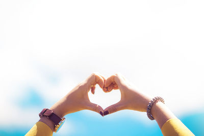 Midsection of woman making heart shape against sky