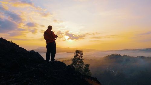 Silhouette man standing by mountain against sky during sunset