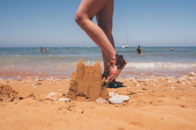 Low section of woman walking on beach against sky