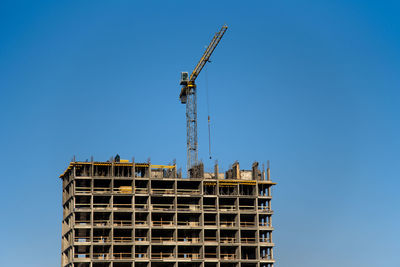 Low angle view of crane by building against clear blue sky