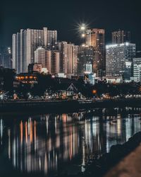 Illuminated buildings by river against sky at night