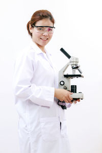 Portrait of young doctor holding microscope over white background