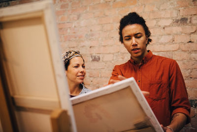 Male and female artists discussing over canvas at art studio