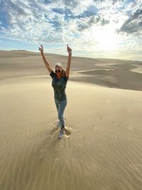 Full length of woman with arms raised standing at desert during sunset