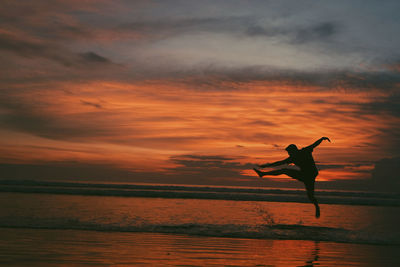 Silhouette man jumping at beach during sunset