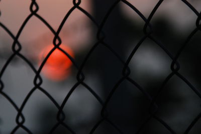 Close-up of silhouette chinlink fence againt sky during sunset