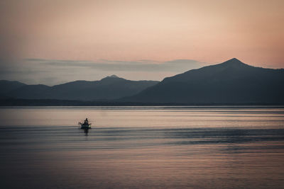 Silhouette person on boat in lake against sky during sunset