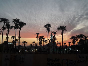 Silhouette palm trees by swimming pool against sky at sunset