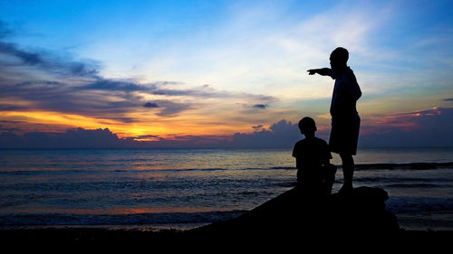 Silhouette man standing at beach against sky during sunset