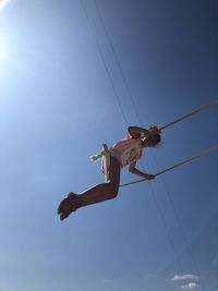 Low angle view of girl sitting on swing against blue sky