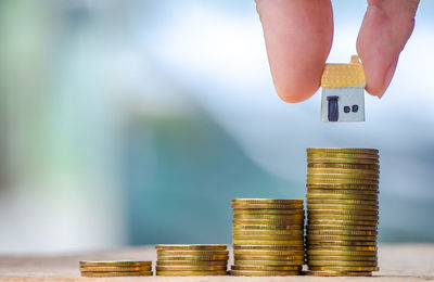 Cropped image of hand holding model house on stacked coins 