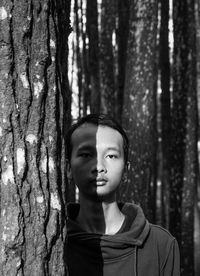 Portrait of young man by tree trunk in forest