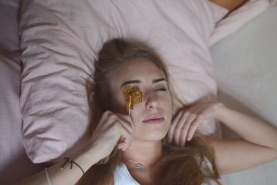 High angle view of woman holding lollipop while lying on bed
