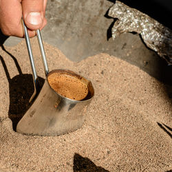 Cropped hand holding coffee in container amidst sand