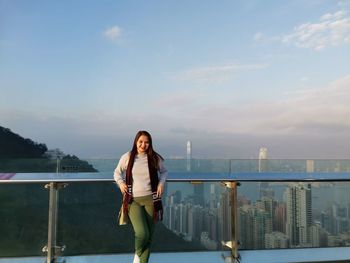 Portrait of young woman standing against railing against sky