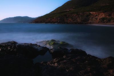 Scenic view of sea and mountains against clear sky