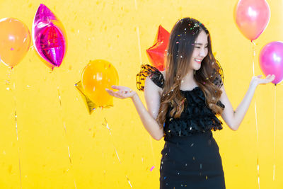 Midsection of woman with balloons standing against yellow wall