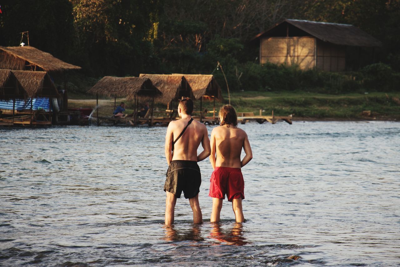 REAR VIEW OF MEN STANDING ON WATER
