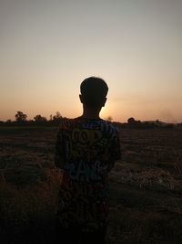 Rear view of boy standing on field against sky during sunset