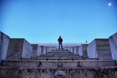 Low angle view of man standing on steps against clear blue sky