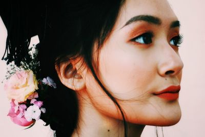 Close-up of beautiful young woman looking away against pink background