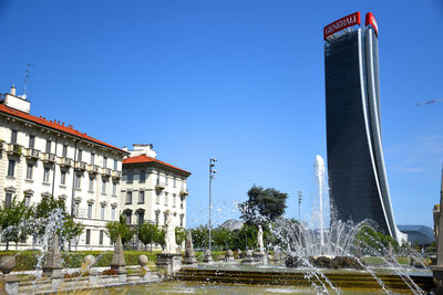 Fountain in city against clear blue sky