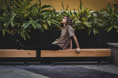 Woman sitting on bench against plants