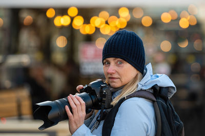 Blonde middle-aged woman with a photo camera in the evening on the city streets, lifestyle concept