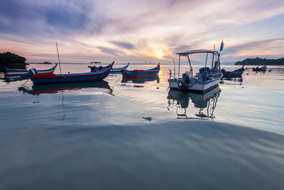 Boats moored in sea against sky during sunset