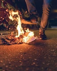 Low section of man standing by burning papers on street at night