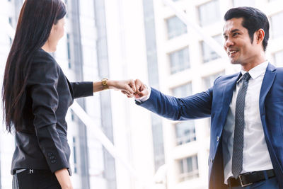 Low angle view of colleagues giving fist-bump while standing against building