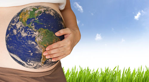 Midsection of pregnant woman with planet earth on stomach against sky