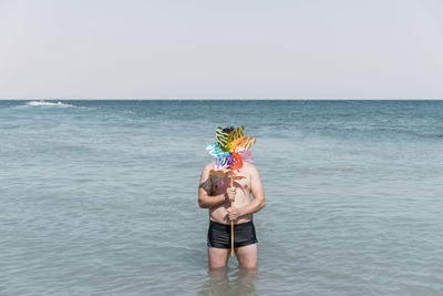 Shirtless man with pinwheel toy standing in sea