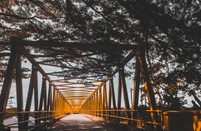 Footbridge amidst trees in forest against sky